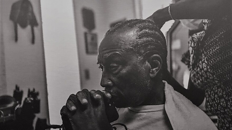 Dallas County Commissioner John Wiley Price having his hair braided by Maurine 'Tootsie' Jones at Tootsie's Braiding Gallery