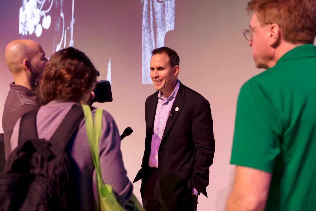 smiling man facing a group of people with microphones