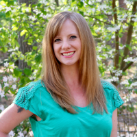 headshot of a smiling woman with brown hair standing in a wooded area