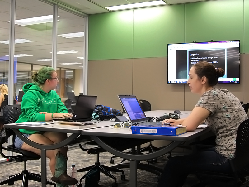 two women with laptops sitting in a study room